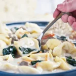 A bowl of hearty sausage tortellini soup with vegetables, garnished with fresh herbs and served with crusty bread