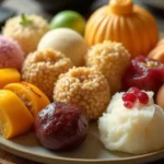 A beautifully arranged platter of traditional Asian desserts, including mochi, sesame balls, mango sticky rice, and red bean buns on a bamboo tray.